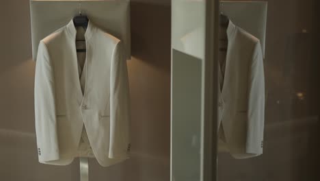 white suit jacket hangs elegantly, reflected in a mirror, waiting for the groom’s special day