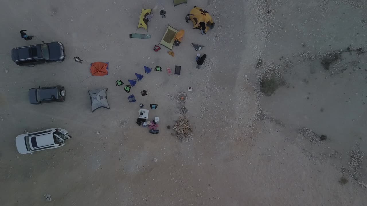 imágenes aéreas de drones de una fogata y campistas con tiendas de campaña en el desierto