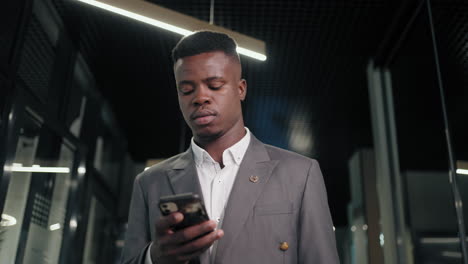 A-black-male-businessman-walks-down-the-corridor-with-a-mobile-phone