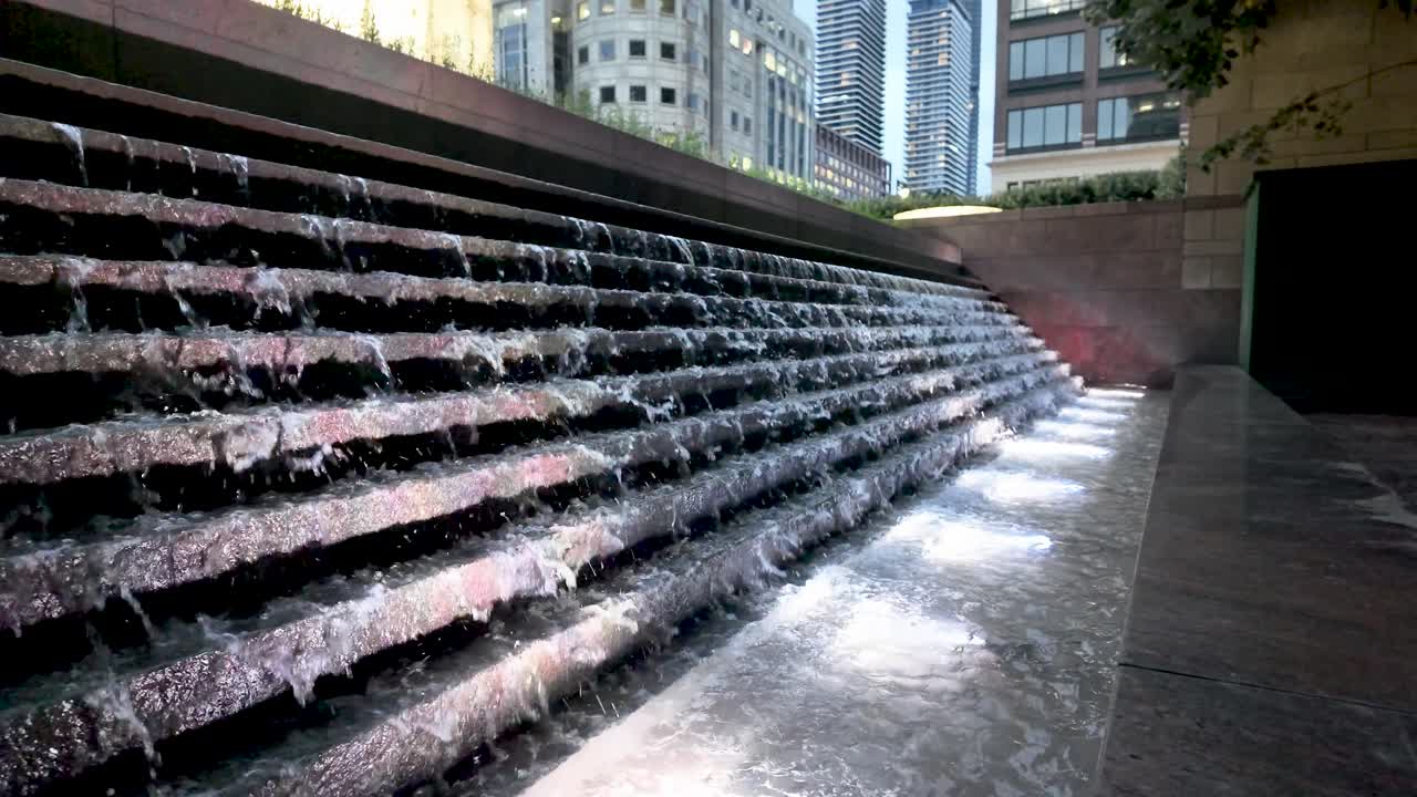 Elegante fuente de agua escalonada con un fondo de paisaje urbano durante el crepúsculo. Cámara lenta.