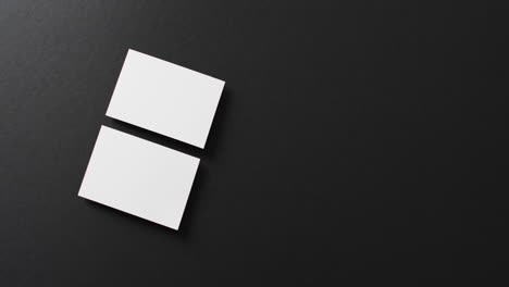 overhead view of two white business cards arranged on black background, copy space, slow motion