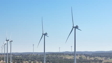 Drone-Past-Row-Of-White-Wind-Turbines-Spinning-With-Rural-Australian-Countryside-Landscape,-Slow-Motion-Telephoto-4K