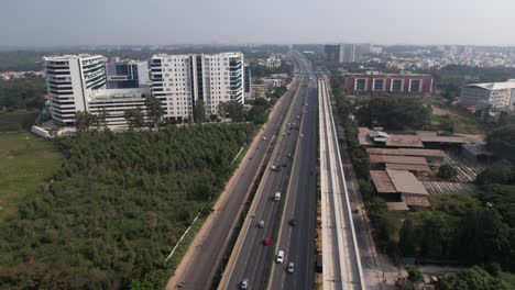 aerial footage of an indian highway that is expanding quickly, with a service road, fast-moving automobiles, and a metro train bridge under construction