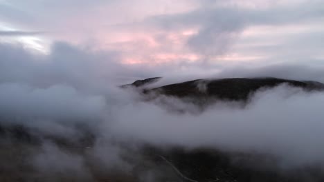 colorful cloudy sunset with the mountains peaking from the clouds drone shot