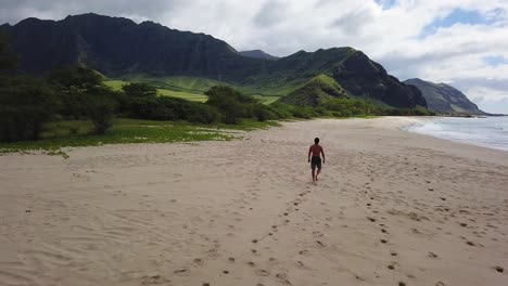 Lone-athletic-man-walks-along-tropical-beach-with-sunlit-mountains