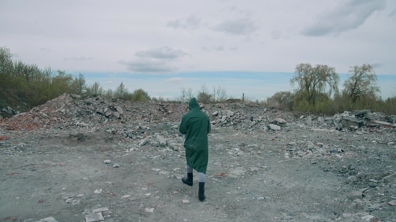 Human in green protective uniform outdoors. Scientist in safety suit walking in ruined place with a high level of radiation. Rear view.