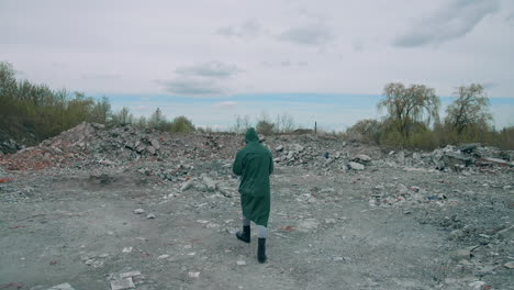 human in green protective uniform outdoors. scientist in safety suit walking in ruined place with a high level of radiation. rear view.