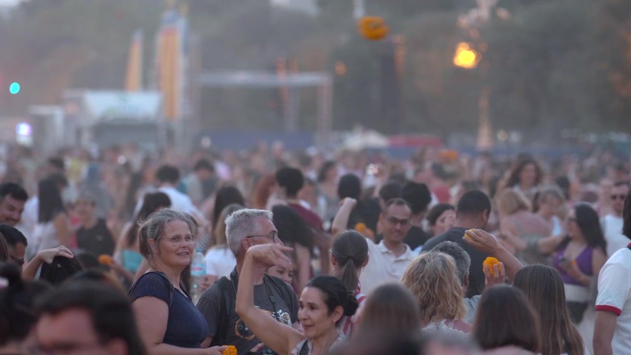 Madrid, Spain, September 10, 2026: Packed outdoor festival crowd from inside audience viewpoint, adults standing close together, raised hands, blurred faces, warm stage lights, dusk haze, and high-energy social atmosphere.