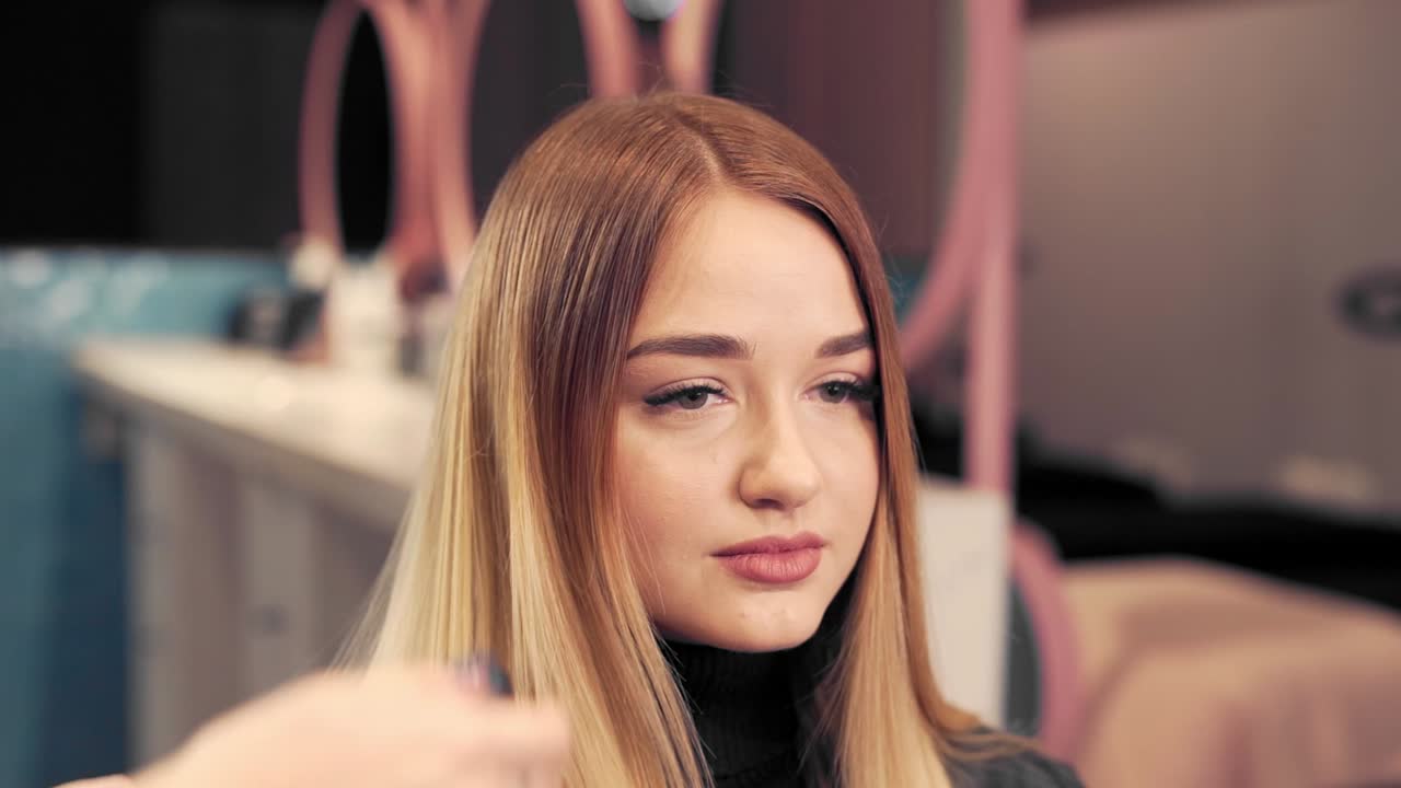 Estilista peina y rocía el cabello de una hermosa chica en un salón de belleza
