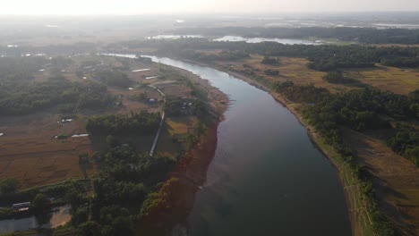 flying above a river in bangladesh, slowly descending down to the water with farmland surrounding and sun reflecting in the water