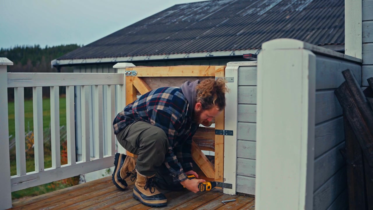 A Man is Using a Power Drill to Install and Secure a Wooden Gate as Part of an Outdoor Fence Construction Project - Medium Shot