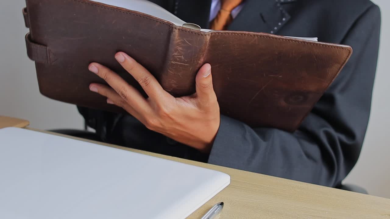 Close up Businessman reviewing notes in vintage leather binder at workspace