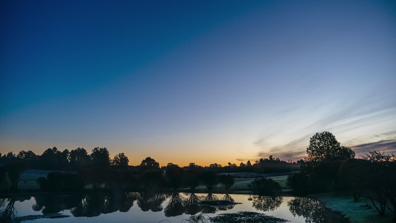 Early morning sunrise timelapse in countryside with fog and dew forming on the ground. Colorful sunrays and clouds in the sky. Rural area of pond, fields and forest. Nature in Latvia. Dawn in autumn.