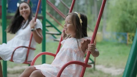 a pregnant mother and her young daughter enjoy playful time together at a playground in the park, surrounded by trees and greenery