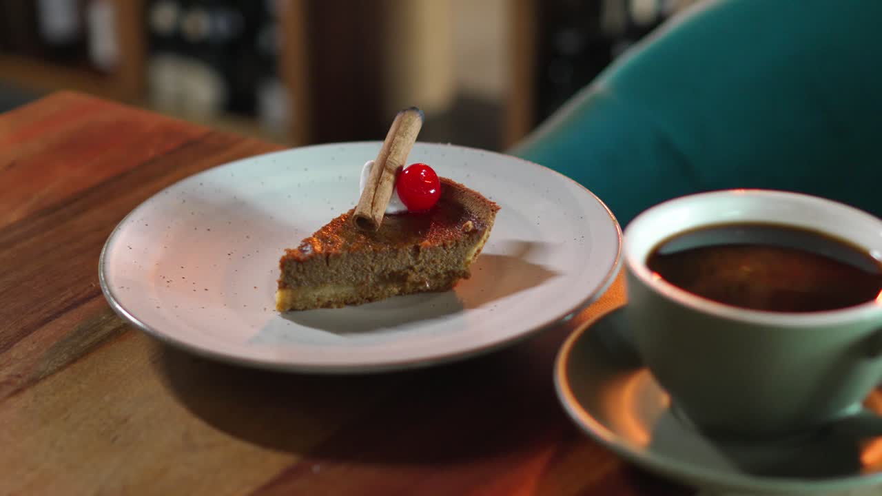 una rebanada de pastel de crema de brownie de calabaza con canela y cereza junto con una taza de café en la mesa en una cafetería