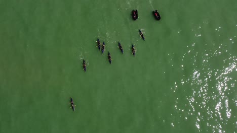 vista aérea de drones toma giratoria de un equipo de remo de kayak deportivo practicando con botes negros en el océano en un día soleado