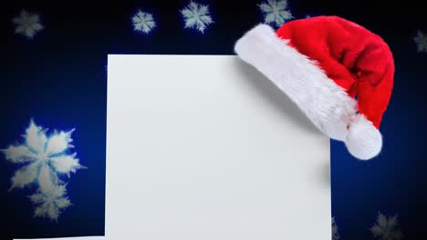 Santa-hat-over-a-blank-placard-against-snowflakes-floating-on-blue-background