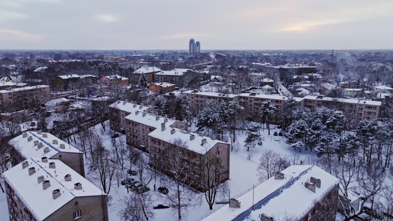 Slow aerial view of snow-covered Soviet-era apartments in Riga, sunset skyline