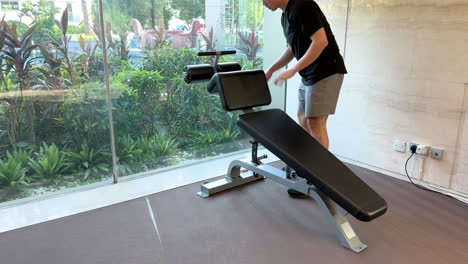 asian man in his 20s adjusts decline bench and performs sit-ups in a luxurious gym