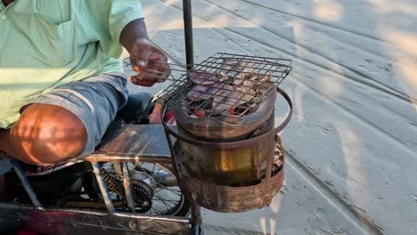 vendor grilling squid on a portable charcoal grill.