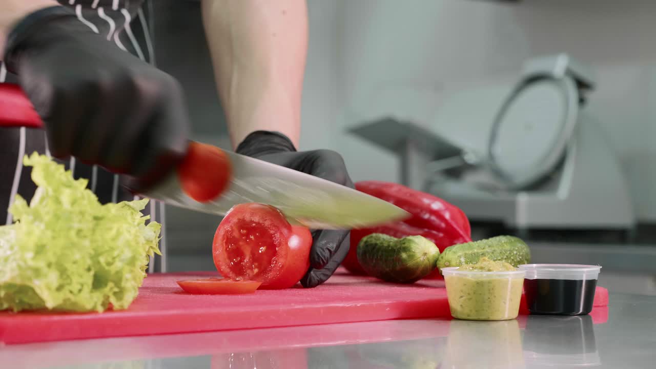 el chef está cortando tomate para la hamburguesa, con las manos en guantes negros de cerca.