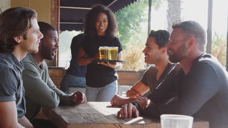 camarera sirviendo bebidas al aire libre a un grupo de amigos masculinos que se reúnen en un bar deportivo