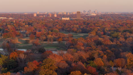 aerial push towards gold course and park with church steeple and city skyline in autumn