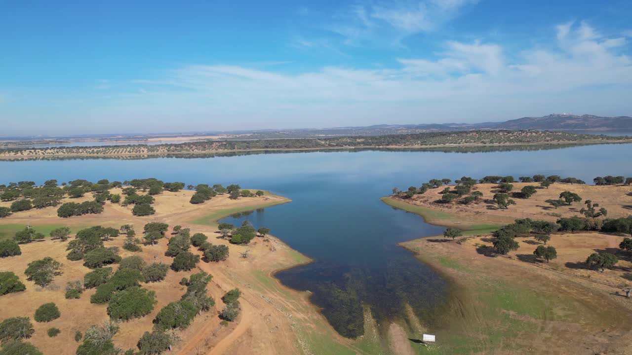 Aerial view of the expansive Barragem do Caia reservoir in Portugal's Alentejo region. Rolling hills and scattered trees meet the tranquil blue waters. For nature, travel, and landscape projects.