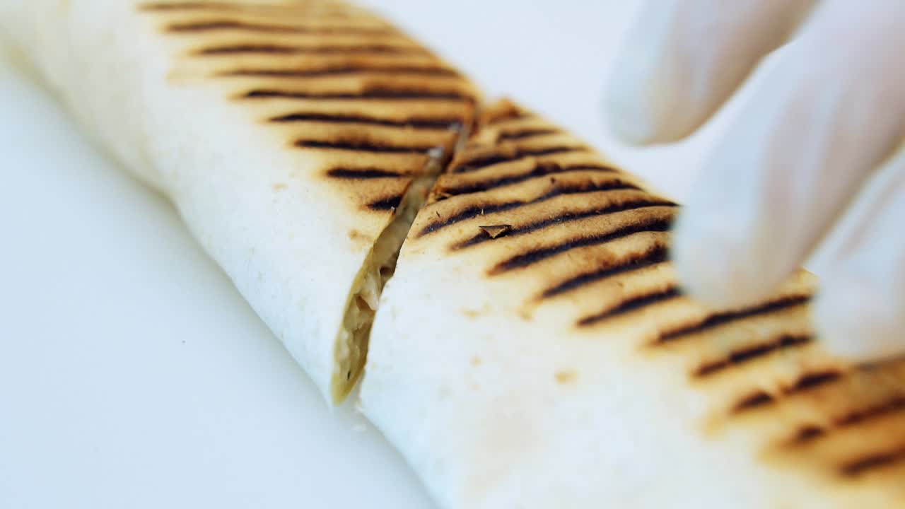 Chef cuts ready shawarma at a restaurant. Hands of the cook cutting rolled pita into two pieces. Tasty snack preparation. Macro shot