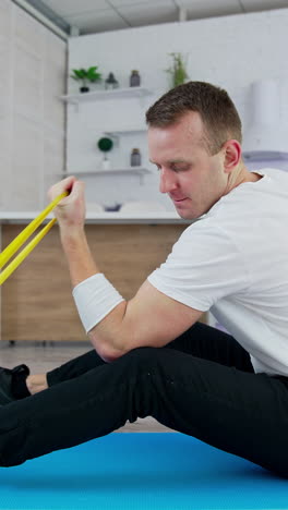 man doing exercises at home. man sitting on the floor at home and doing exercises with spander. vertical video