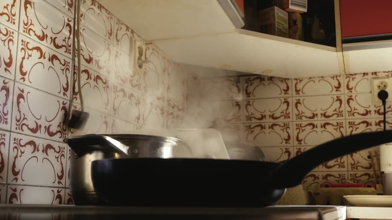 A person pours oil into a pot and then stirs the food with a wooden spoon in a pan that is smoking