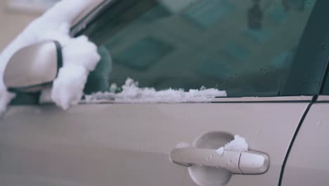 snow lies on car with folded rearview mirror and front door