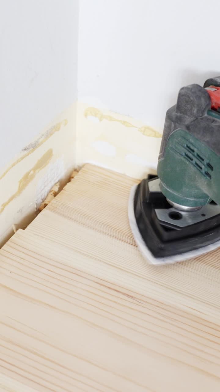 Utilizzo di una levigatrice di dettaglio per levigare un angolo del pavimento in legno. Inquadratura verticale