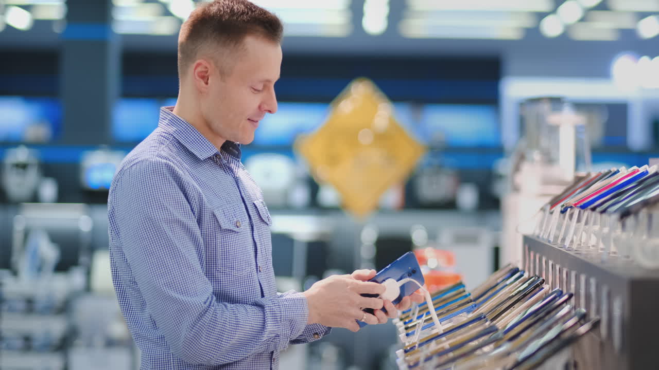 A young handsome man standing at a shop window with smartphones in a portable electronics store chooses to buy a new phone model. Purchase the latest version of the gadget