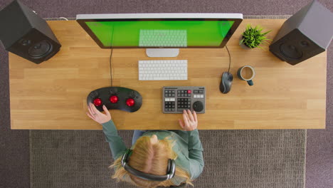 overhead view of female video editor working at computer with green screen in creative office