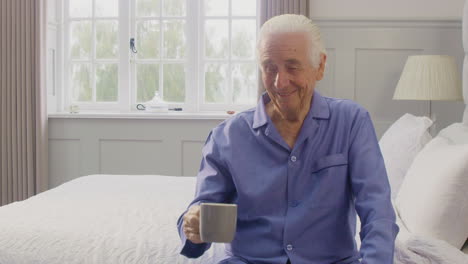Älterer-Mann-Zu-Hause-Im-Pyjama,-Der-Auf-Dem-Bett-Sitzt-Und-Morgens-Eine-Tasse-Tee-Trinkt