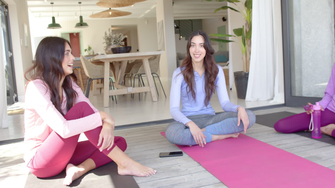 Women friends relaxing on yoga mats at home, enjoying conversation and laughter
