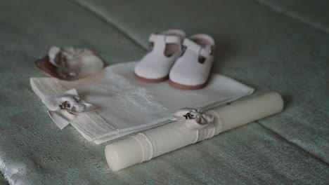 christening set with baby shoes candle embroidered cloth and bonnet arranged on soft fabric