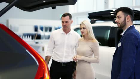 car agent showing trunk to customers car in automotive dealership showroom