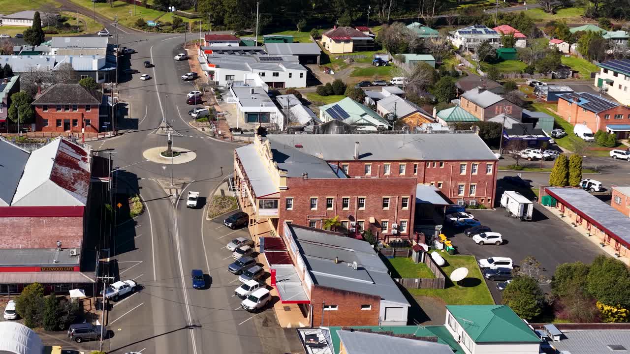 Drone ascends above Dorrigo, revealing town center, shops, cars, and residential streets in daylight