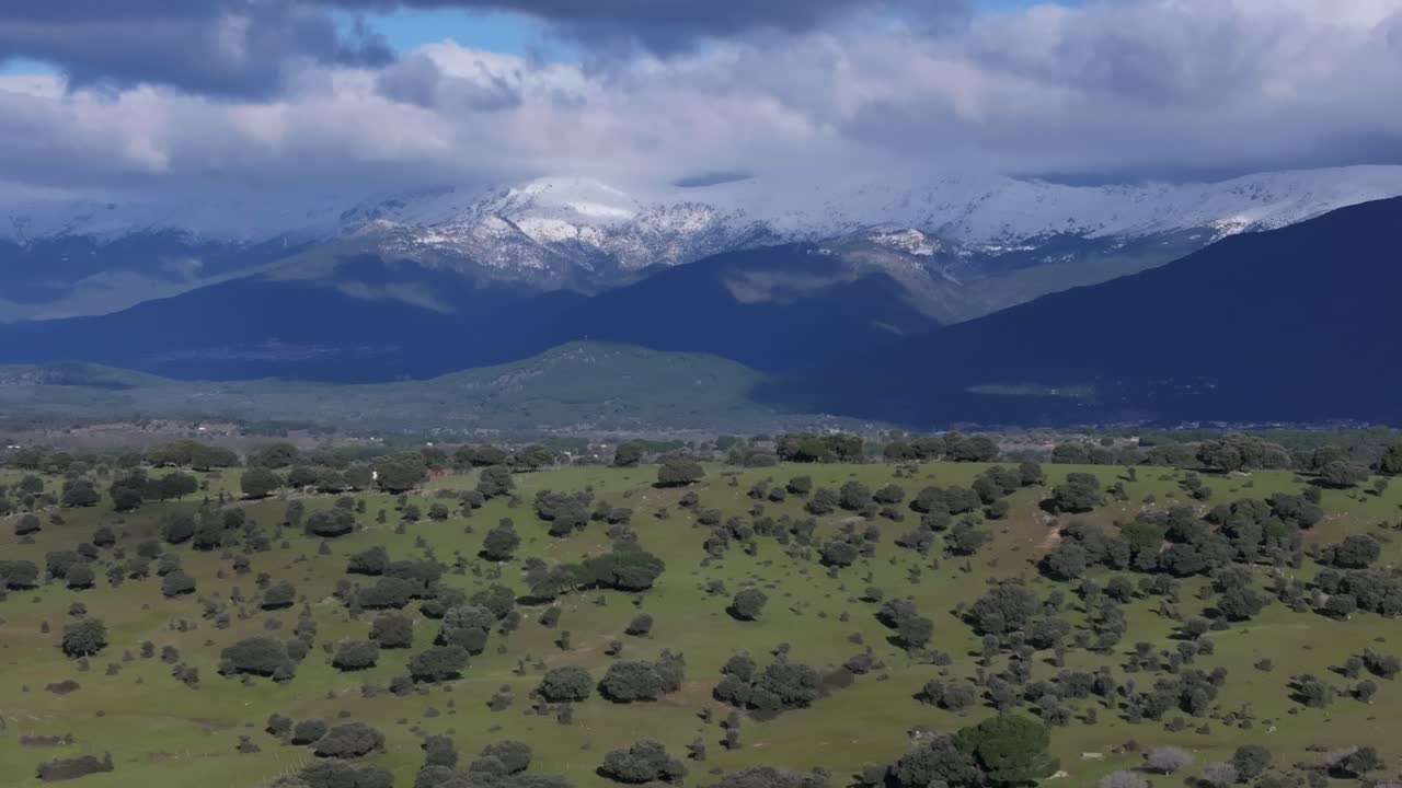vuelo lateral con un dron visualizando una ladera con robles y detrás de las montañas gredos con picos nevados y nubes enganchadas creando un efecto de paralaje valle de tietar ávila españa