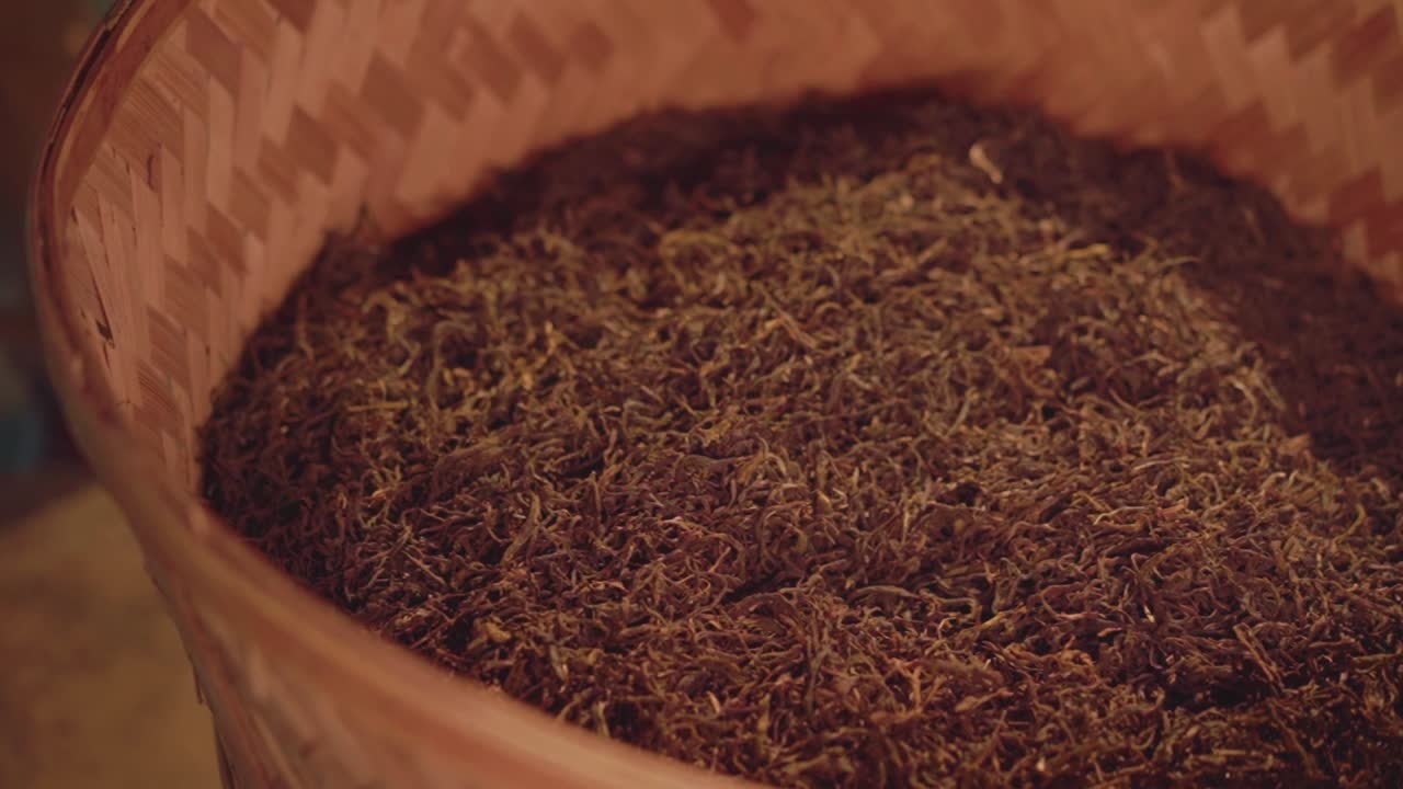 A woven basket filled with dried tea leaves is opened, revealing the rich texture inside. Great for themes of organic tea production, slow food, and artisanal process.