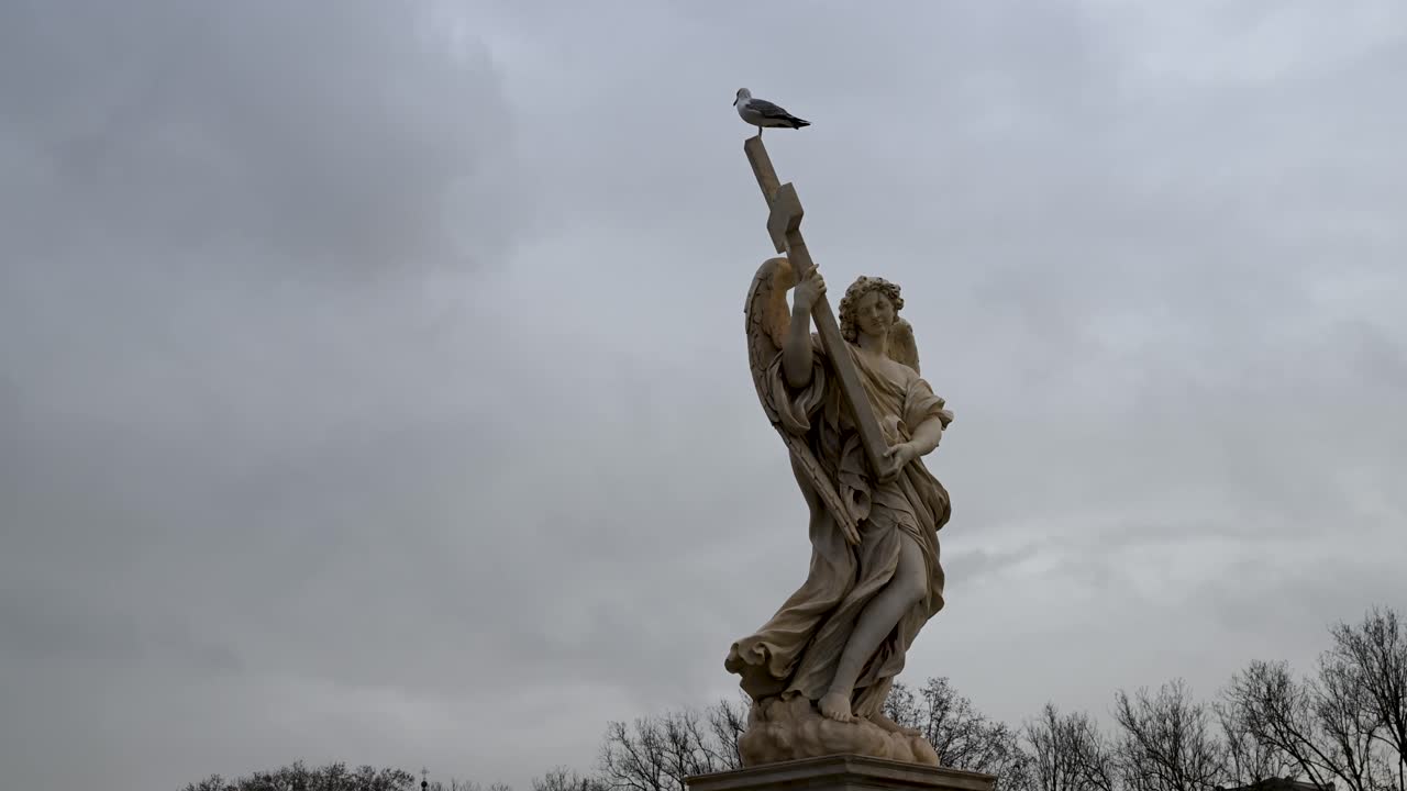 Una vista dettagliata dell'angelo di marmo che tiene la croce, scolpito per il Ponte Sant'Angelo come parte della collezione Bernini, con vista sul fiume Tevere.