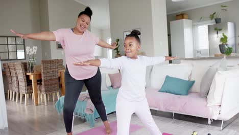 happy unaltered african american mother and daughter doing yoga stretching at home, slow motion