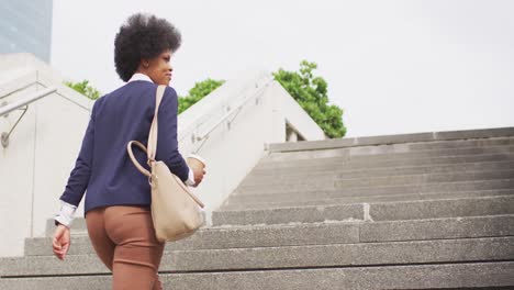 african american businesswoman holding takeaway coffee and walking