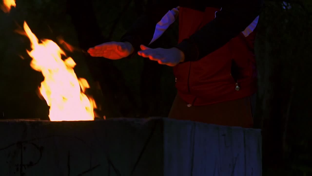 밤에 밖에 있는 화로에 담긴 불에 손을 따뜻하게 하는 사람