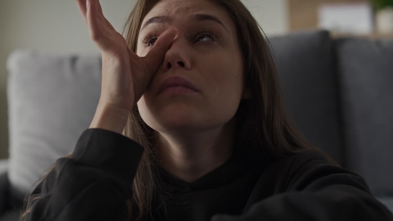 una mujer caucásica sentada en el suelo y llorando en casa.