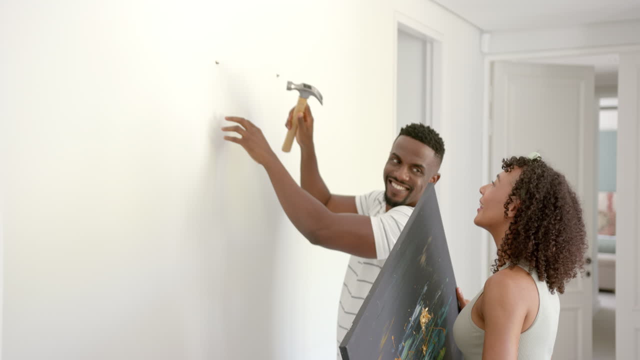 Hanging artwork on wall, couple decorating home together, smiling and enjoying time