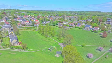 Drone ascent above Shibden Park, Halifax, revealing a broad green landscape with cherry trees, a visible playground, paths, and the surrounding town architecture, slow motion