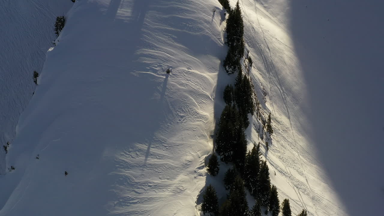 vista aérea volando a lo largo de una cordillera cubierta de nieve en los alpes franceses en invierno, con sombra y luz matutina